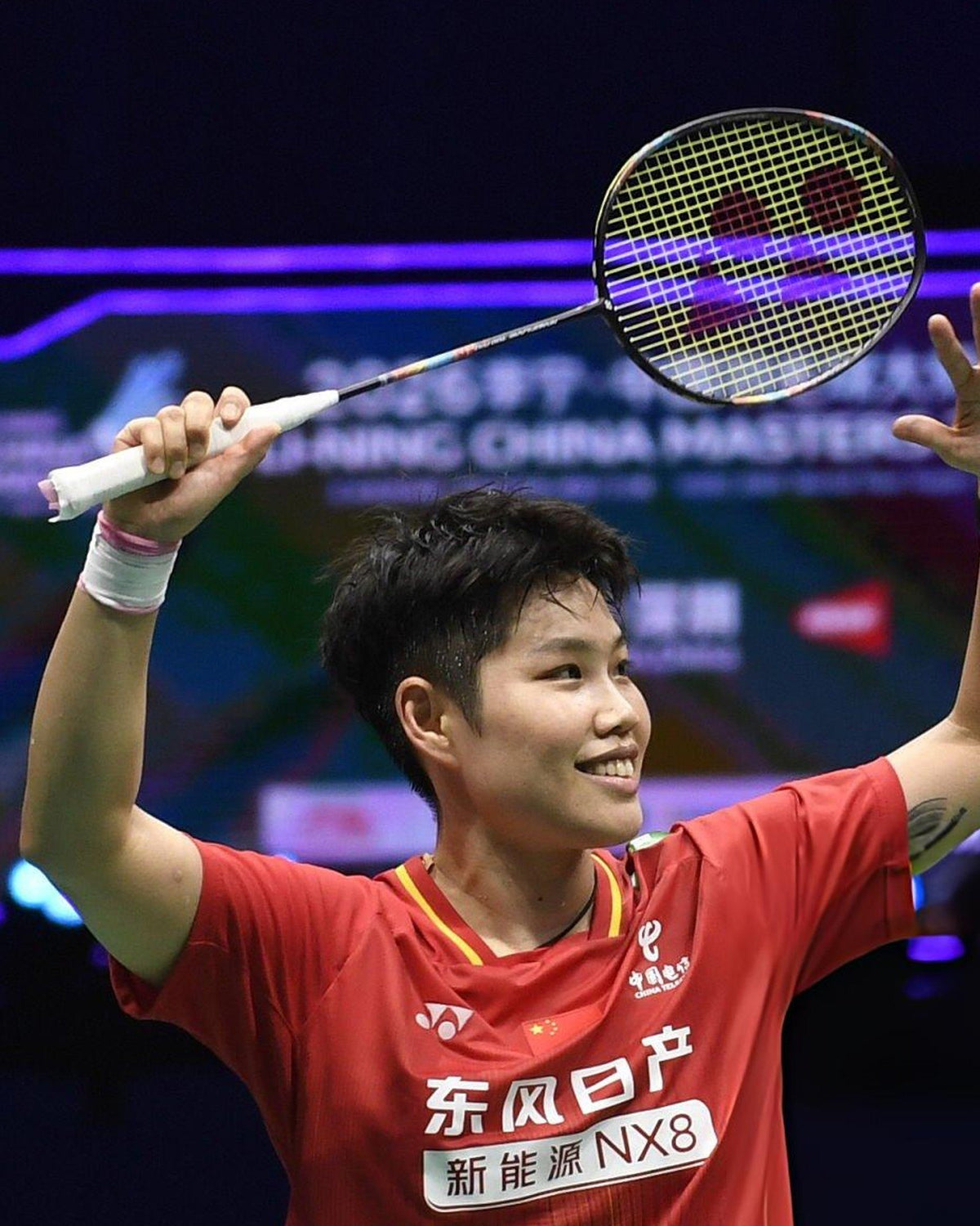Huang Dongping smiling with her Yonex badminton racket raised overhead