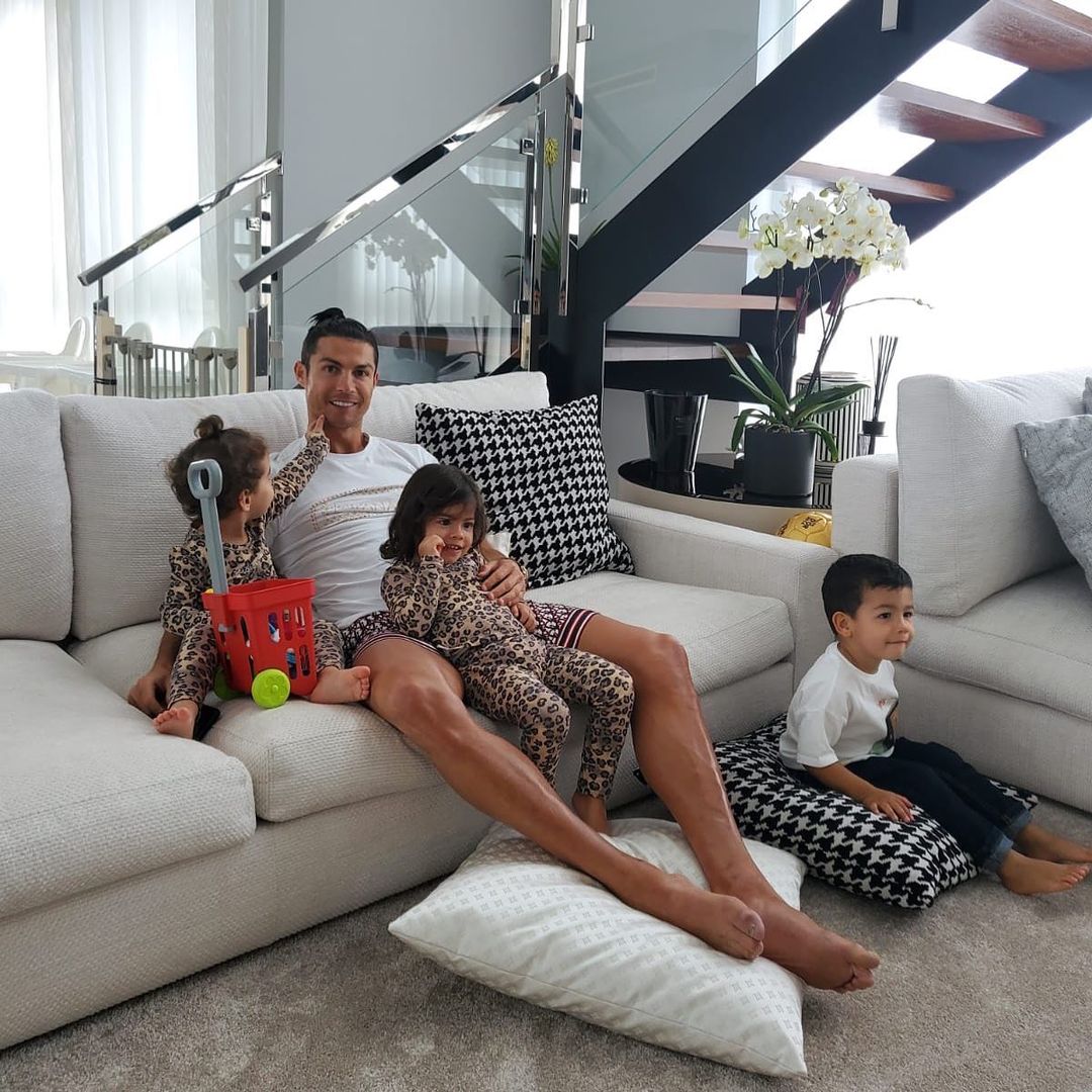 Cristiano Ronaldo seated on sofa with two baby girls and one boy.